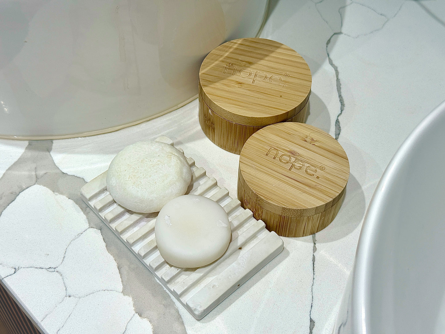 Scouse Bird Shop diatomite dish with two solid shampoo bars on a marble countertop.